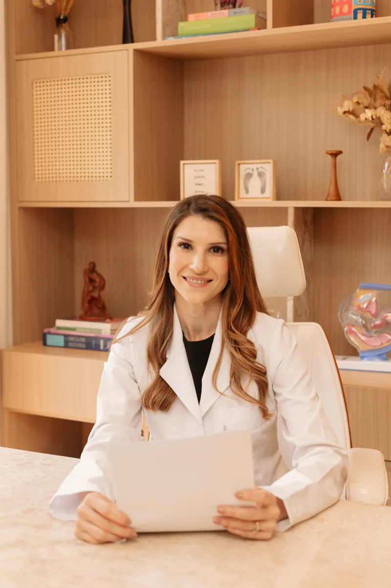 Dra. Camila Cinquetti sentada à mesa do consultório, de jaleco branco